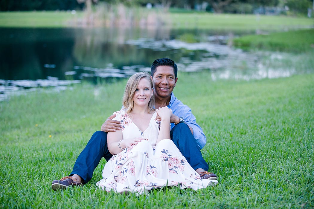 couple sit next to lake in park for photoshoot