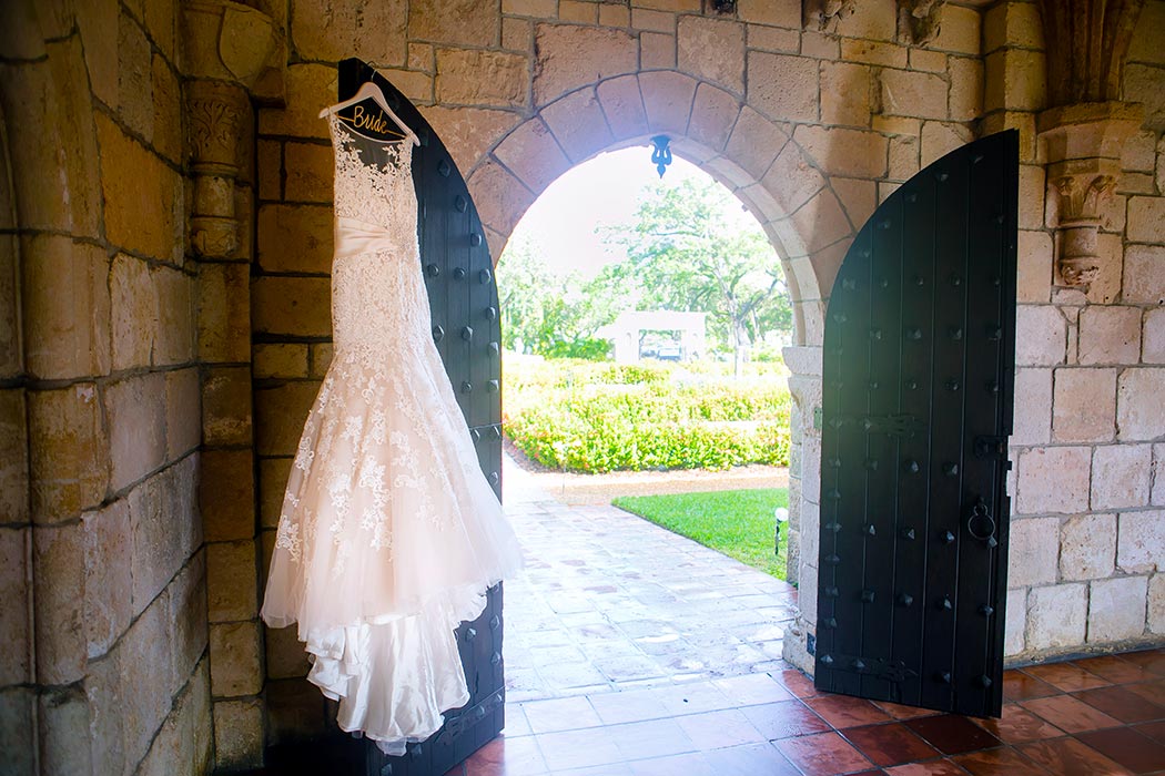 beautiful lace wedding dress hanging on the door of ancient spanish monastery | miami wedding photographer