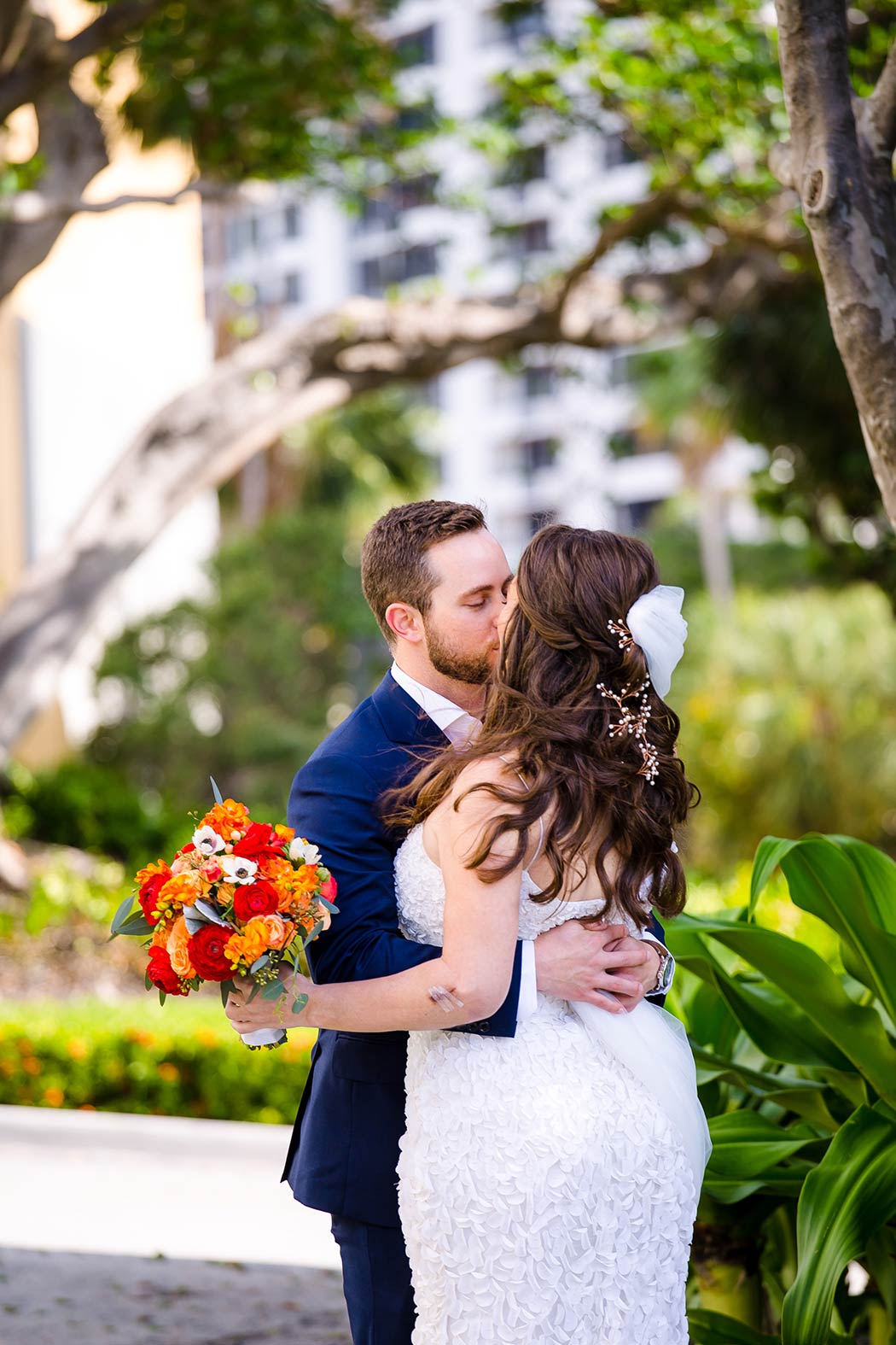 bride and groom kiss after their first look in a miami park | red and orange rose bouquet