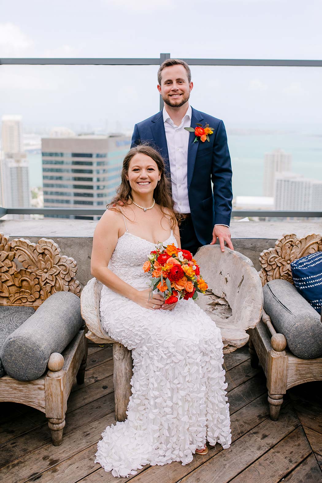 bride and groom pose on chair at east hotel miami wedding | orange and red wedding bouquet