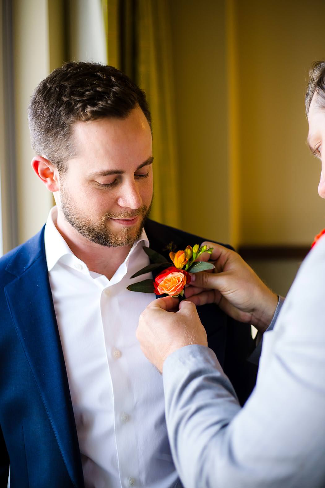 groomsmen puts on grooms red and orange boutonniere before jewish wedding at east miami