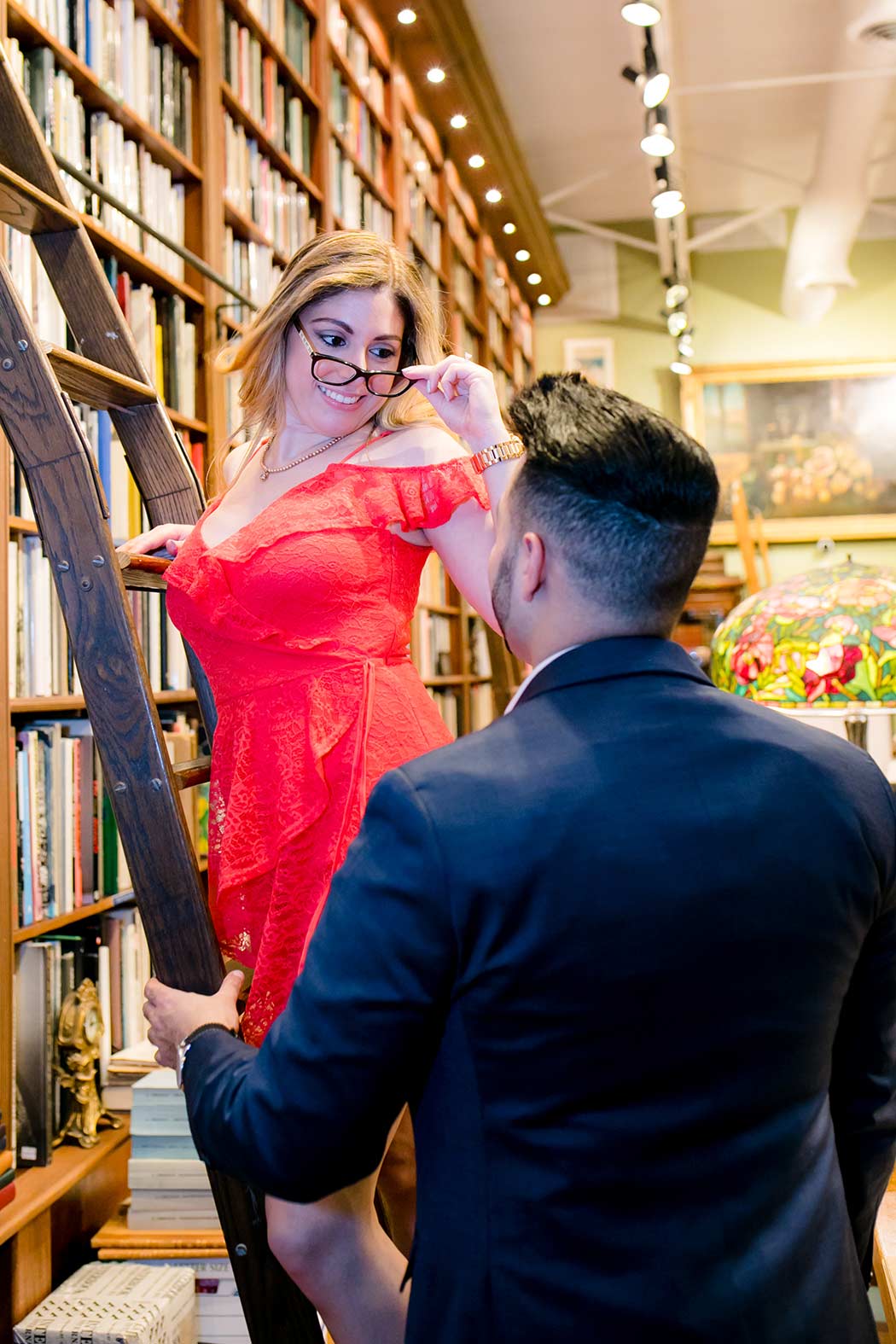 couple pose on library ladder in book store for their engagement session | fort lauderdale engagement photographer