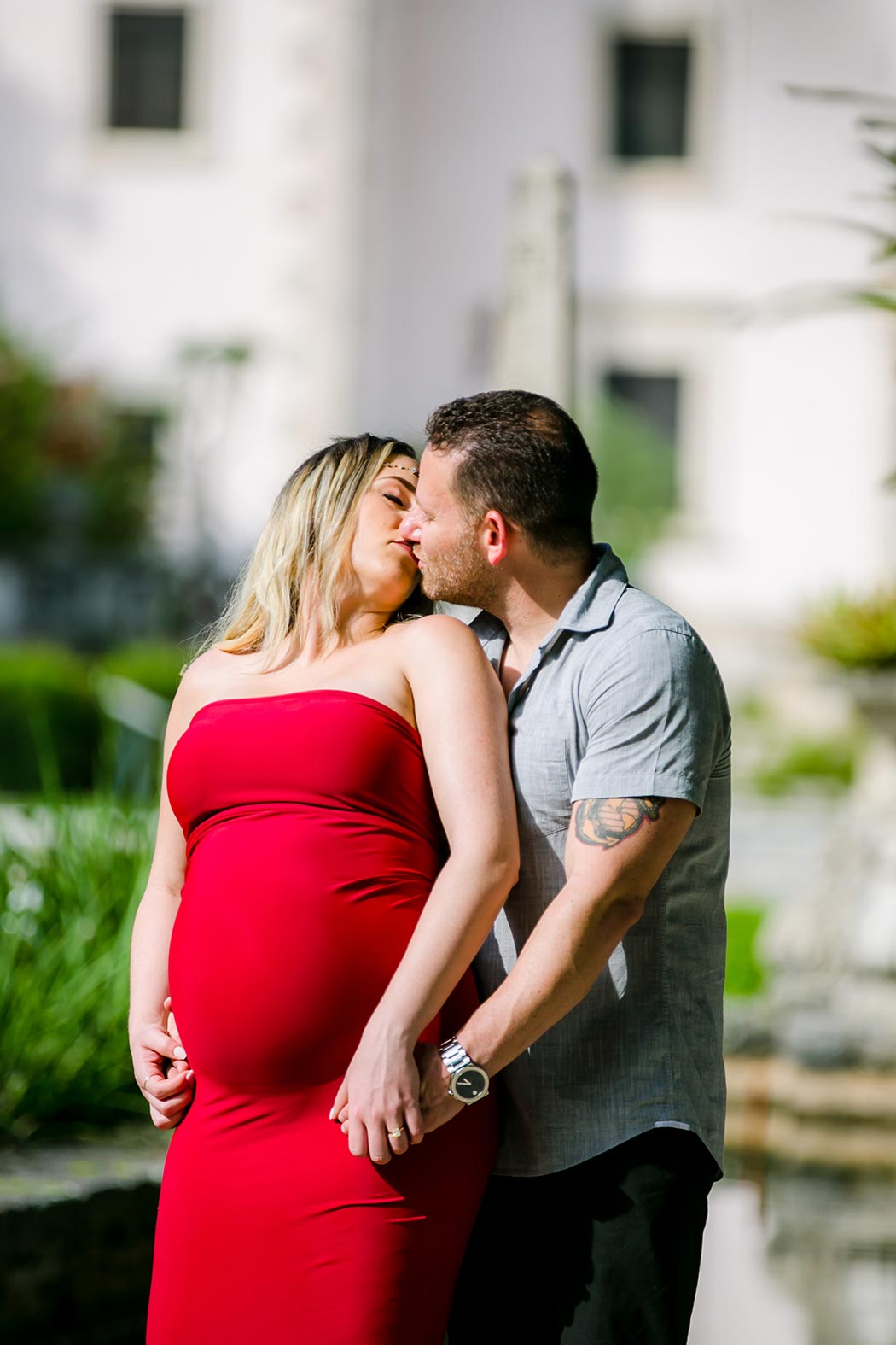 husband and wife kiss during vizcaya museum miami maternity sessoin vizcaya museum and gardens miami elegrant maternity photoshoot with long red dress
