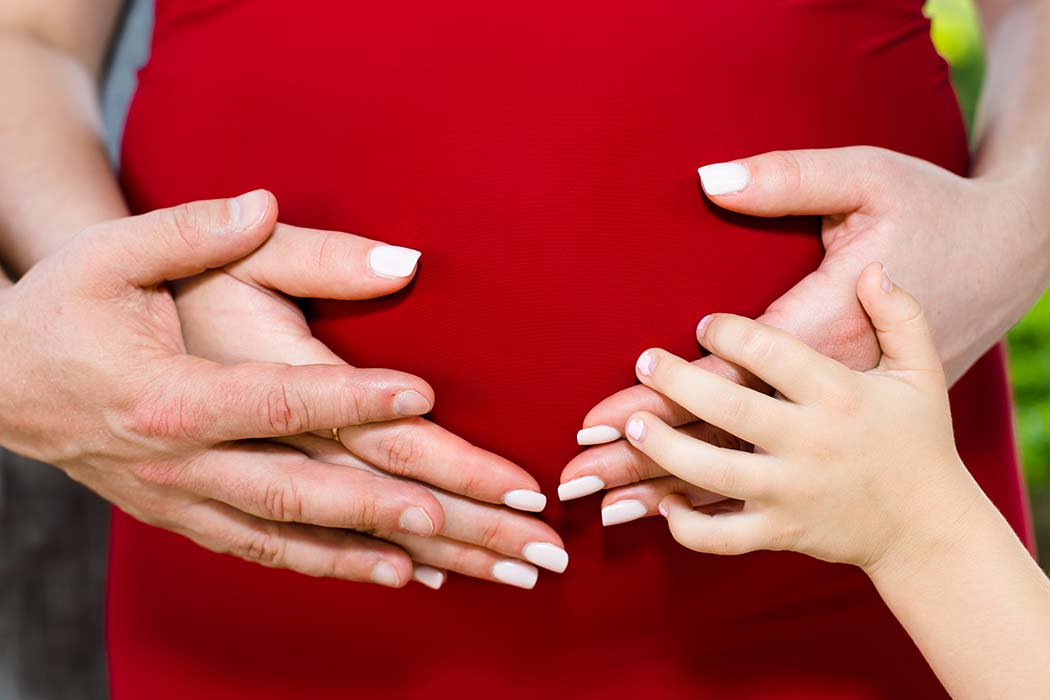 family put hands on belly for this elegant maternity photoshoot with red maternity dress