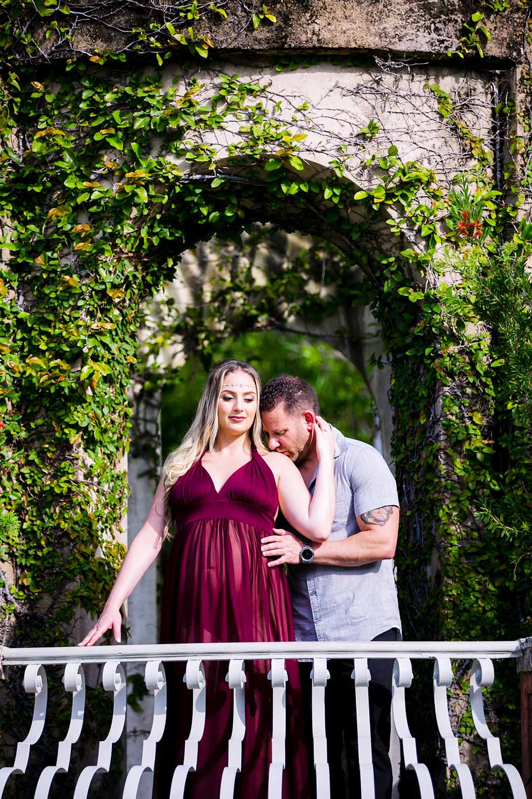 husband kisses wife during elegant maternity session husband and wife elegant maternity session at vizcaya museum | long red maternity dress