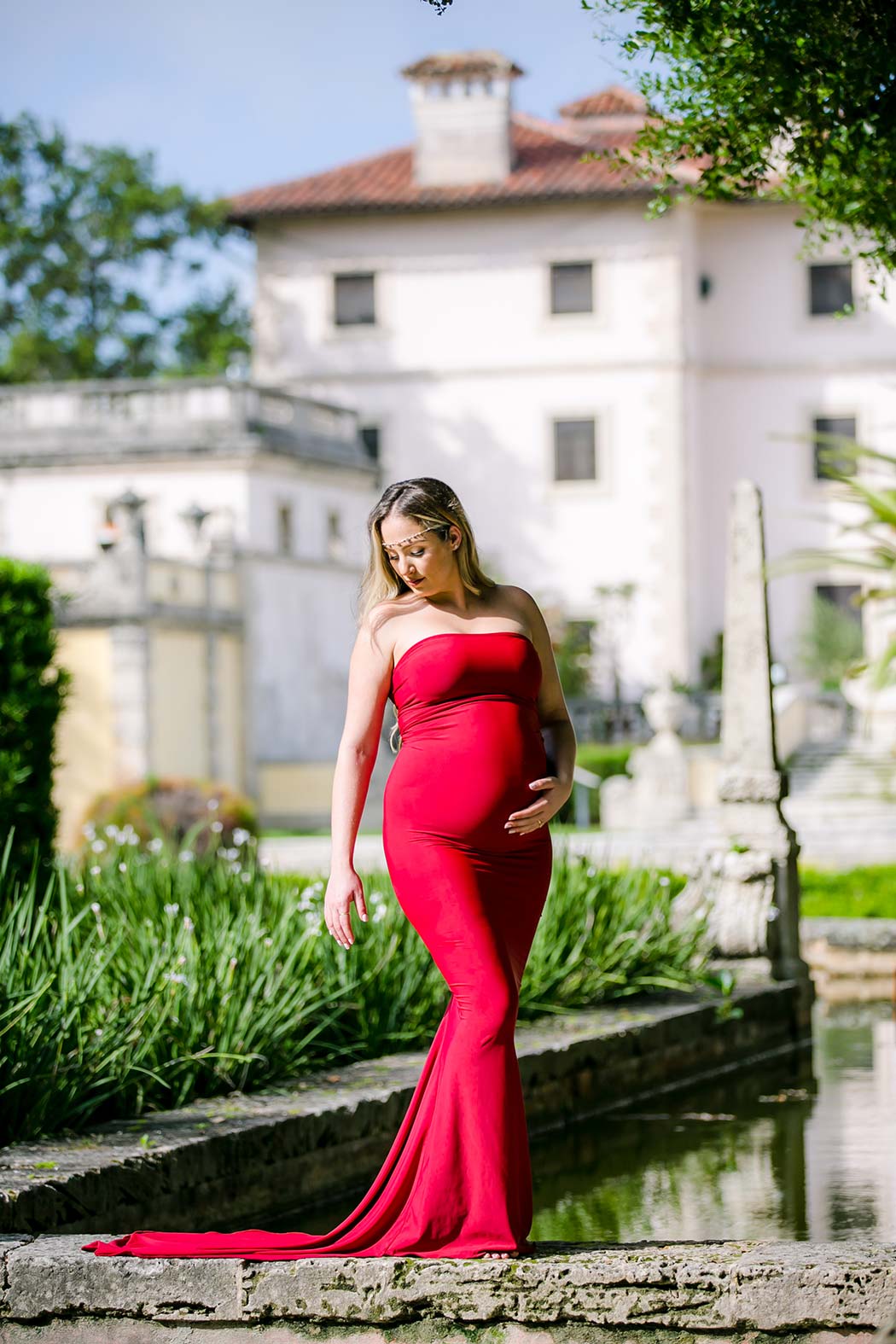 expectant mother elegantly poses in red maternity dress at vizcaya museum elegant red maternity dress for photoshoot at vizcaya | fort lauderdale maternity photographer