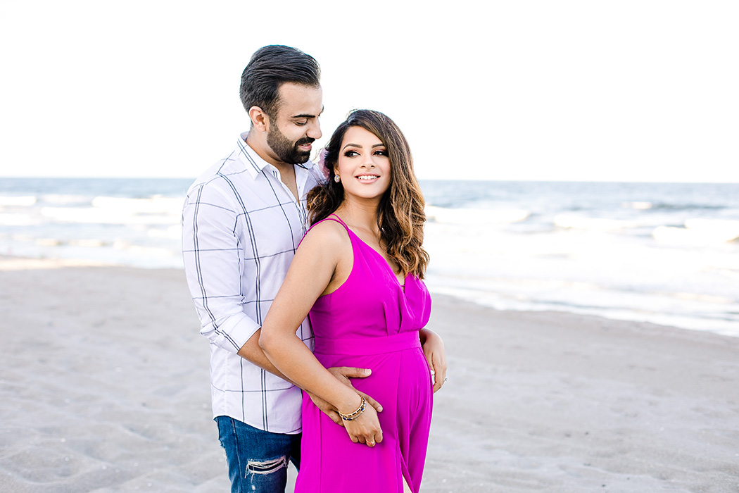 couple posing on the beach for a beach maternity photography session wearing pink maternity dress