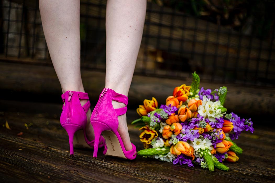 bride wears hot pink high heeled wedding shoes next to an orange and purple wedding bouquet