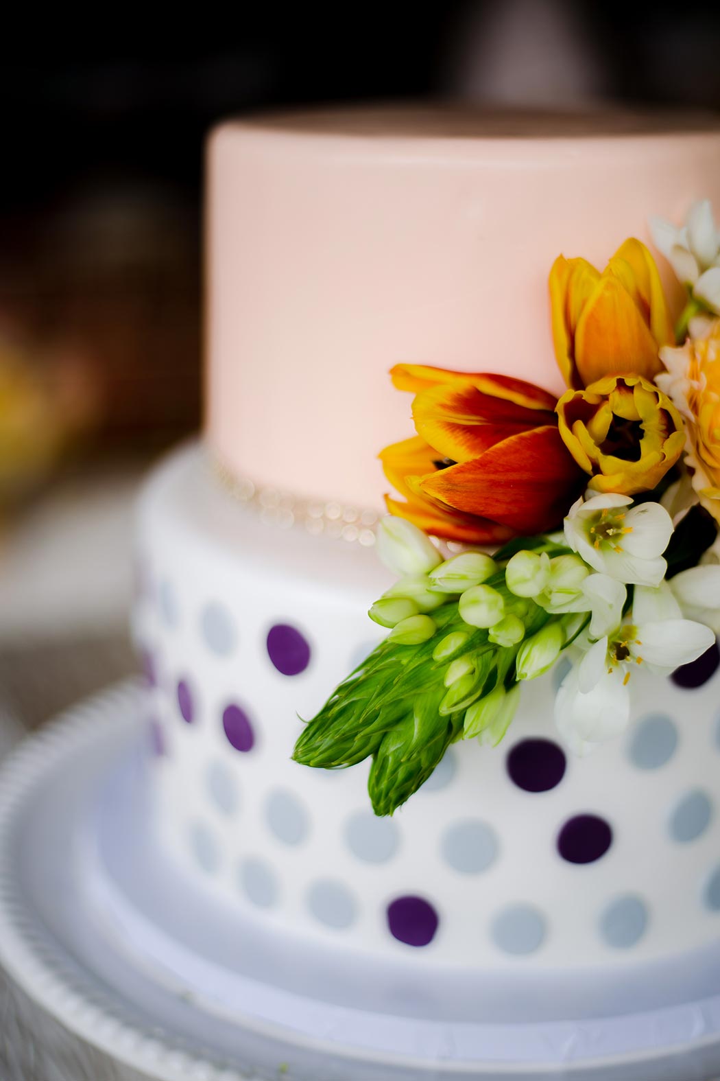 photograph of modern two tier white, purple and orange wedding cake with flower topper
