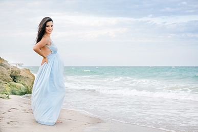 beach maternity shoot wearing blue floor-length maternity dress