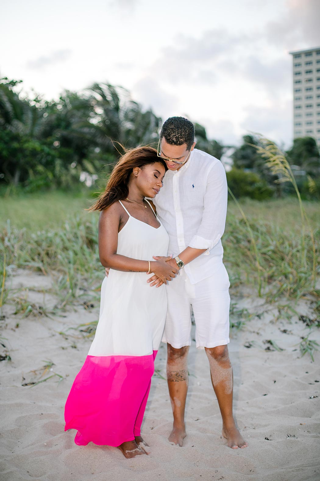 black couple posing on pompano beach during gender reveal photoshoot | white and pink maternity dress
