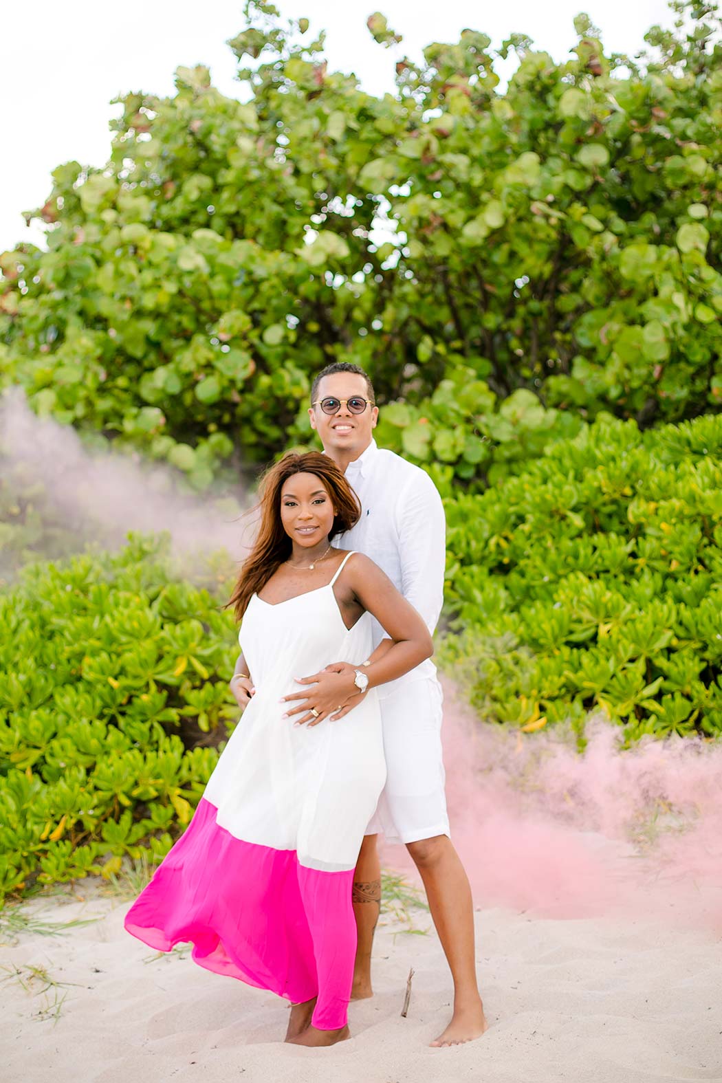 couple pose on the beach for gender reveal photoshoot with pink smoke bomb | south florida maternity photographer
