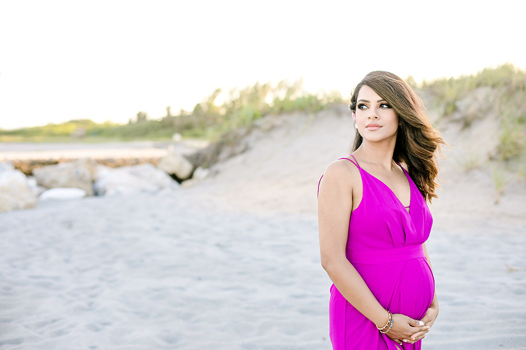 girl in pink maternity dress holds belly during beach maternity photo shoot in fort lauderdale